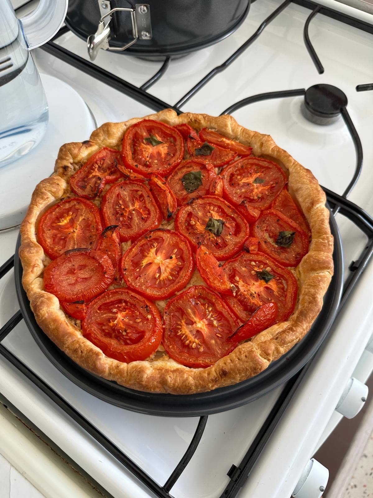 A golden puff pastry tart topped with roasted tomato slices and basil.