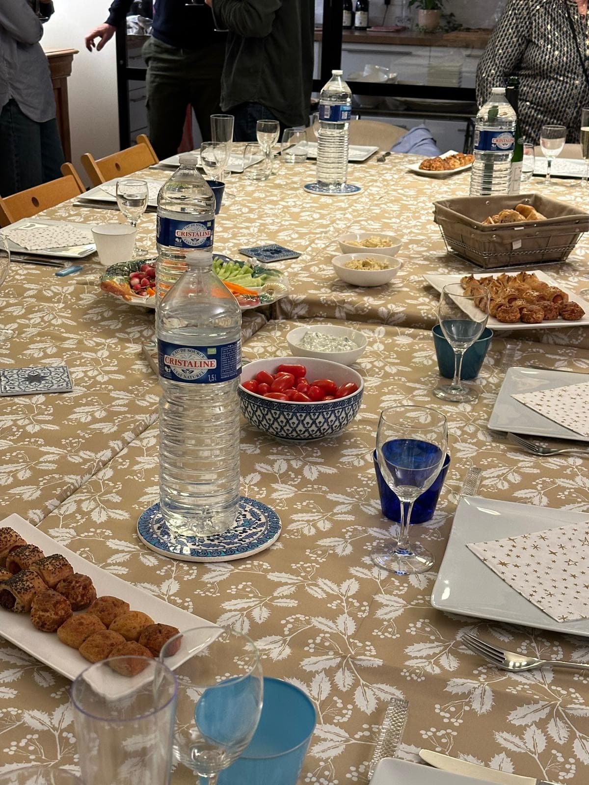 A long table with a patterned tablecloth, glasses, water bottles and plates of snacks.